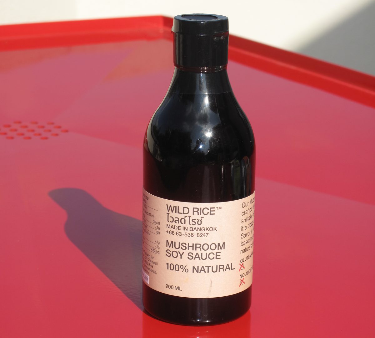 Bouteille de Mushroom Soy Sauce Wild Rice posée sur une table rouge